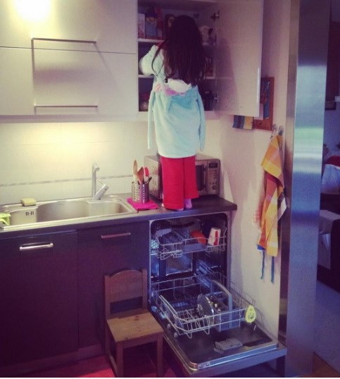 Μικρό κορίτσι σκαρφαλωμένο σε πάγκο κουζίνας ψάχνει σε ανοιχτό ντουλάπι
