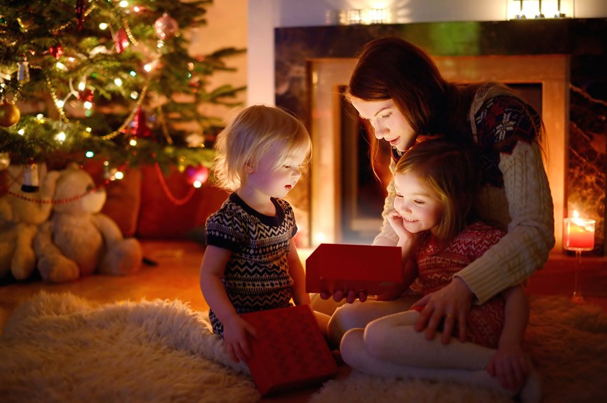 Μαμά με παιδιά ανοίγουν τα δώρα με φόντο το χριστουγεννιάτικο δέντρο